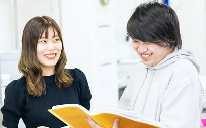資料を開いて笑顔で打ち合わせをする二人のスタッフ